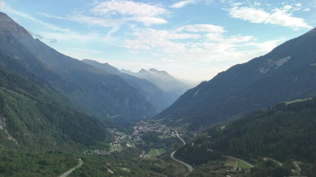 Aerial drone view of a deep alpine valley with a village and winding road near San Bernardino, Switzerland