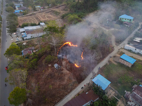 Aerial view of a small brush fire burning on a hillside near residential houses and a road in Waisai, Southwest Papua, Indonesia.
