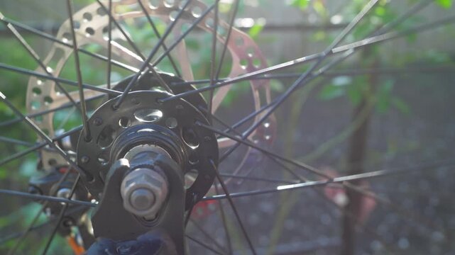 Spinning bicycle wheel moves fast making spokes and hub appear blurry. Metal parts shine as wheel rotates. Repairs bicycle upside down outdoor, small business. Sun lights through spokes