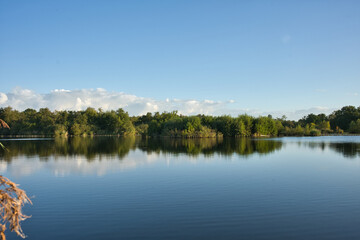 Obraz premium Clear blue sky and fluffy white clouds reflected in the calm, mirror-like waters of a lake in Loosdrecht, Netherlands
