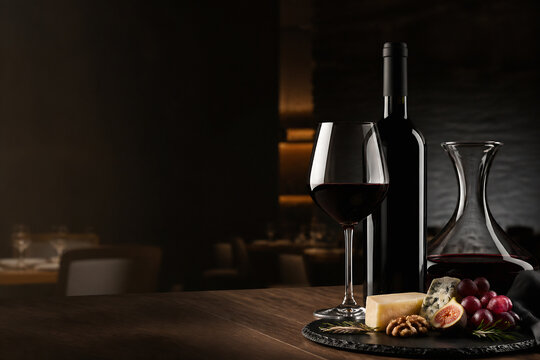 A still life of a glass of red wine, a bottle, cheese, grapes, and a decanter on a dark wooden table in a dimly lit interior.