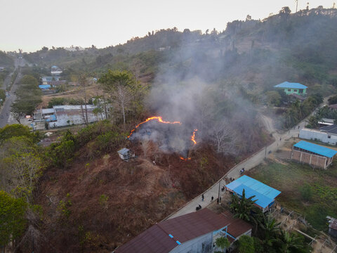 Aerial view of a brush fire burning on a hillside near residential buildings and a road in Waisai, Southwest Papua, Indonesia.