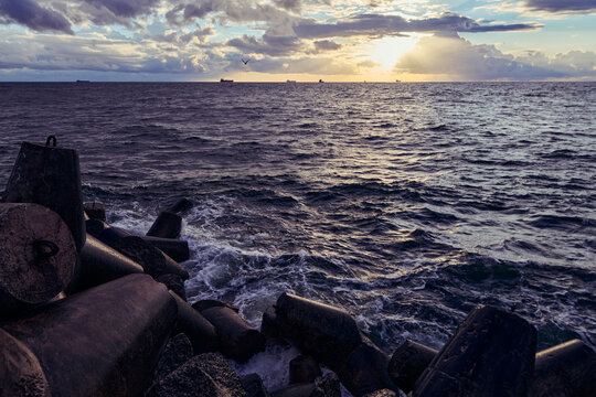 Ocean waves break against coastal concrete barriers at sunset