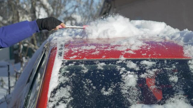 Man brushes packed snow from red car windshield before departure. Dense winter cover hides glass surface and reduces visibility. Subzero weather creates challenge for safe vehicle access