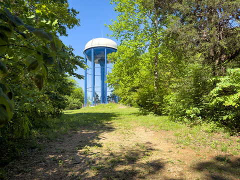 Horizontal view of blue water tower framed by trees, seen from low angle along a grassy trail