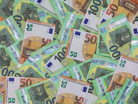 Many 50 and 100 euro banknotes overlapping in a top-down view. Cash background.