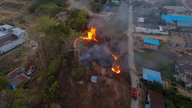 Aerial view of a fire burning on a hillside near Waisai, with a fire truck parked on the adjacent road and nearby residential buildings in Raja Ampat, Southwest Papua, Indonesia.