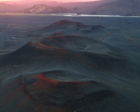 Aerial view of Icelandic Highlands volcanic craters with dark volcanic soil and reddish hues under sunset light in Iceland.