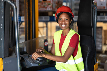 Young female warehouse worker smiling at camera, wearing safety vest and hard hat, driving a forklift in a logistics center © Dejan