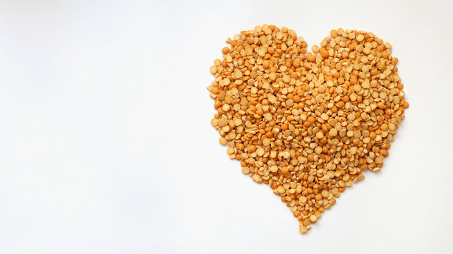 Heart made of dried yellow split peas on white background with copy space. Healthy Food and Plant Protein. Overhead view.