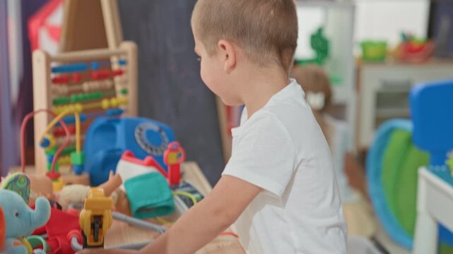 Boy in white t shirt playing with abacus and assorted toys, hand moving beads and picking up a doll inside a daycare building; childhood curiosity.