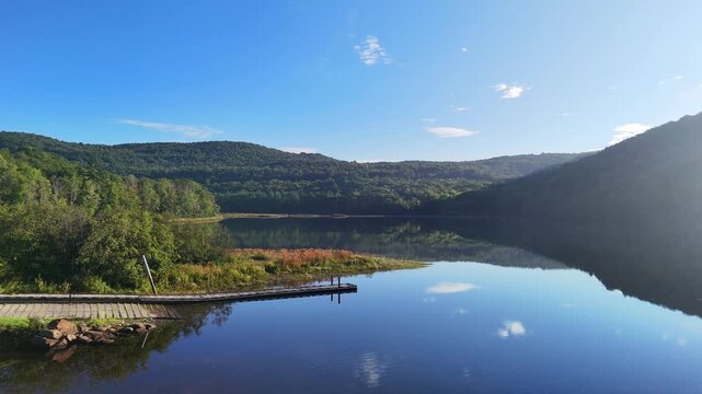 Peaceful nature and boating recreation. Scenic water slow dolly drone view at Sherman Reservoir Boat Launch, Vermont, USA, with forested mountains, tree reflections and clear sky. 4K.