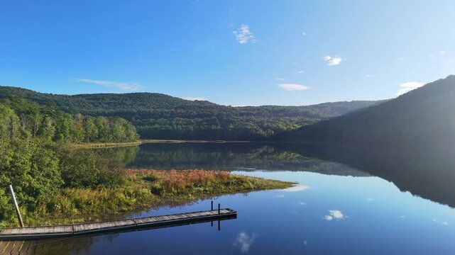 Scenic water slow dolly drone view at Sherman Reservoir Boat Launch, Vermont, USA, with forested mountains, tree reflections and clear sky. Peaceful nature and boating recreation. 4K.