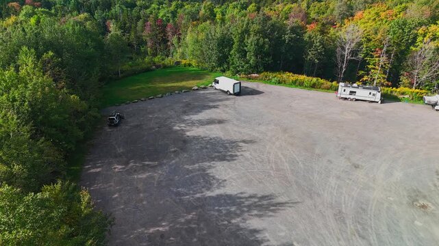 Aerial view of gravel parking area with campers and trailers near Hogback Mountain Conservation Area forest in early September autumn, representing rural travel and recreation.