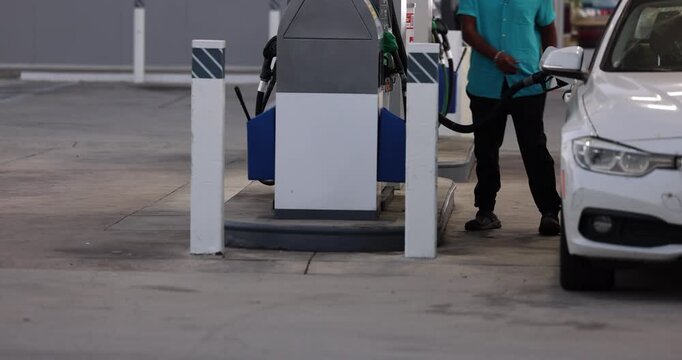 An individual disconnects a gas hose from a car and reconnects it to a gas pump at a gas station.