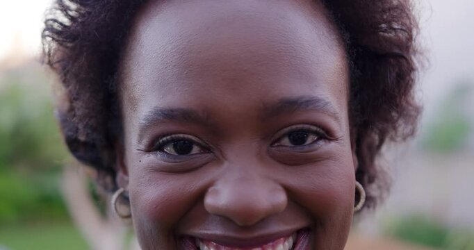 African woman smiling widening grin and laughing facing camera in garden wearing hoop earrings
