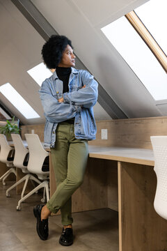 African man leaning on long bench in loft workspace, wearing denim jacket, observing skylights