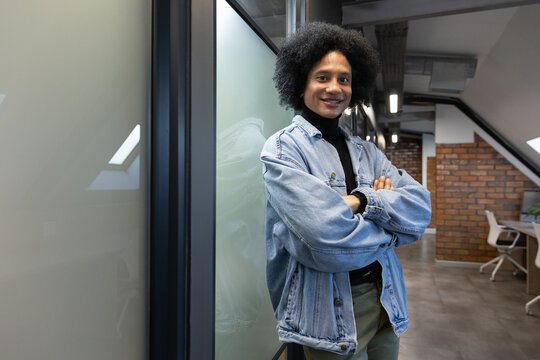 Man leaning against frosted glass partition wearing denim jacket, crossing arms in modern office