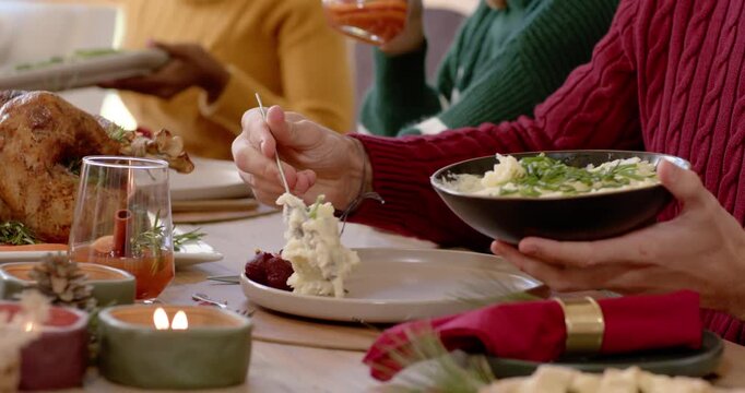 As meal is starting, red sweater server is scooping mashed potatoes onto plate at dining table