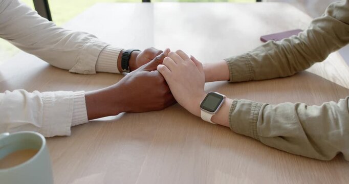Hands are meeting, interlacing and squeezing after placement on wooden table, showing care with cup