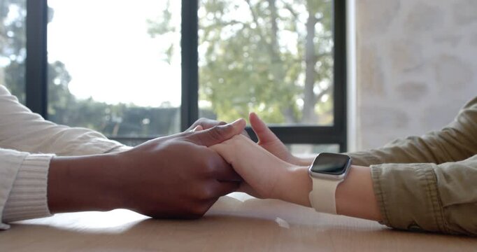 Left hand reaching to touch right hand, fingers interlacing stroking for comfort on wooden table