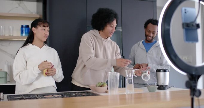 African trio at kitchen island center reaching for pitcher pouring into cup filming with ring light