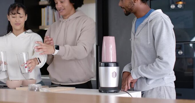 Diverse group in hoodies prepping glasses while right man plugging blender in kitchen for drinks