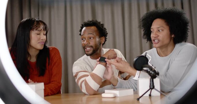 Diverse co-hosts showing smartwatch at studio table, phone showing livestream sparking demo