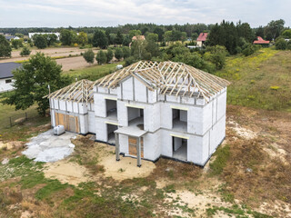 Etap budowy domu jednorodzinnego z widoczną więźbą dachową, położonego w malowniczej, wiejskiej okolicy. Ujęcie z drona pokazuje postęp prac oraz otaczający krajobraz. © Leszek Szelest