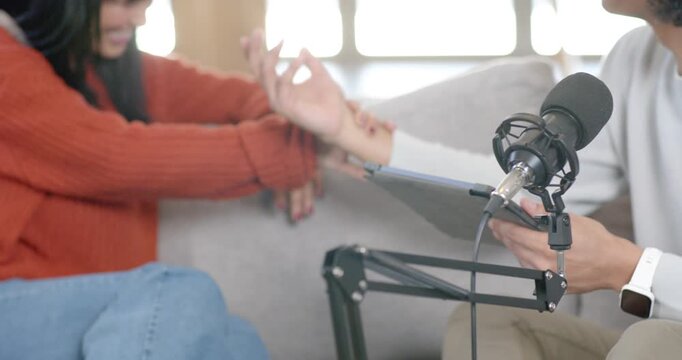 Diverse cohosts recording on couch, woman in rust sweater while right host holding tablet near mic