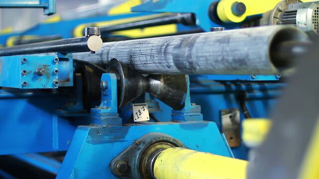 Metal tube moving through roller conveyor. Closeup pipe production line factory.