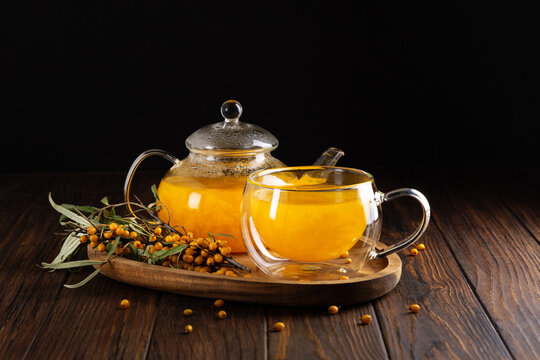 Glass teapot and cup filled with bright orange sea buckthorn tea served with fresh berries on a wooden tray