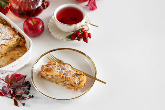 Delicious apple strudel slice served on white plate with golden trim next to tea and fresh apple
