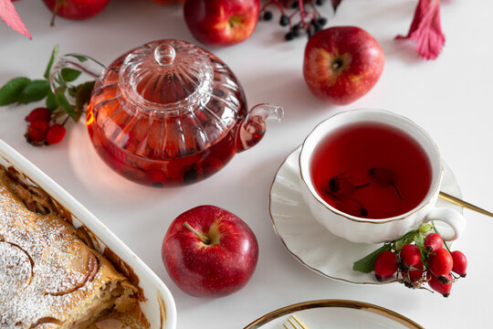 Autumn apple pie and tea served with fresh apples and rosehips on white table