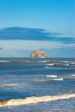 Coastal landscape featuring Bass Rock volcanic island and lighthouse with copy space in blue sky.