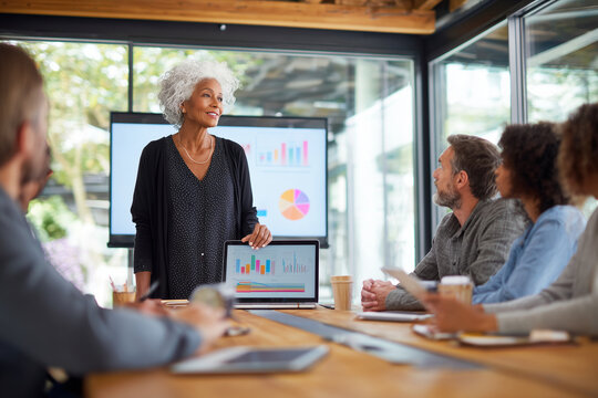 Senior African American Female Executive Explaining Laptop Data To Young Diverse Team In Modern Office