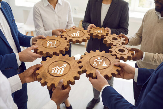 Diverse business team connecting wooden gears with growth and collaboration symbols in modern office.