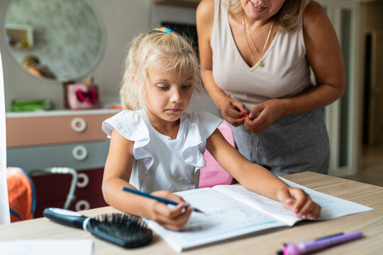 Mother supervises her daughter homework independent learning at home. School education, family relationship and childhood routine