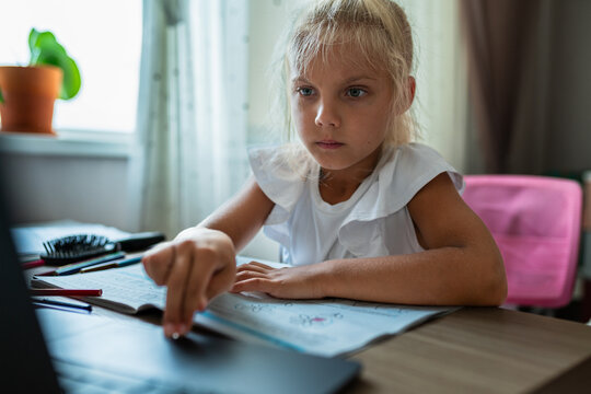 Elementary school student studies at home with a laptop and workbook. Distance learning, home education and digital technology