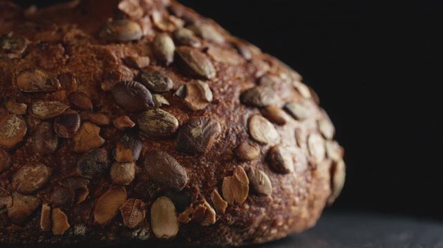 Close-up of artisan whole wheat sourdough bread topped with pumpkin seeds on a dark background. Freshly baked organic loaf with crispy crust for commercial bakery promotions and healthy food concept.