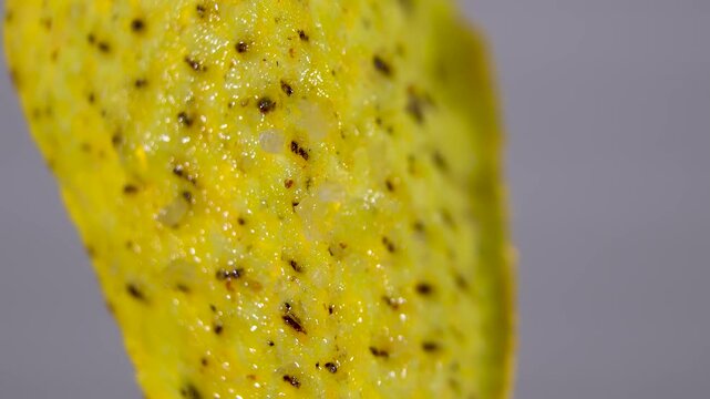 Rotating triangular corn nacho chip surface with seasoning on grey background, macro