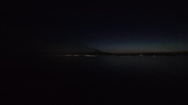 28 April 2026 Italy, Sicily, Strait of Messina - sunset till darkness timelapse cruise ship passing coastline and mountain range and hills