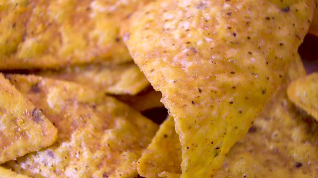 Single seasoned corn nacho chip rotating among a pile, extreme macro