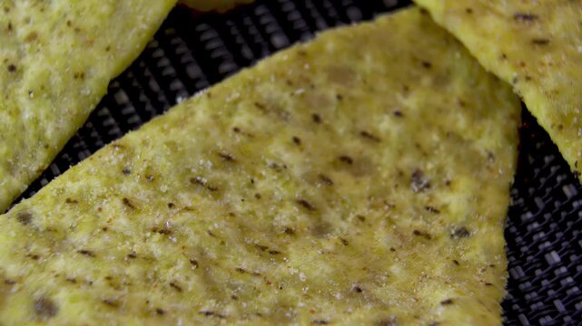 Seasoned triangular corn nacho chip rotating on dark textured background, macro