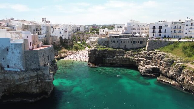 Polignano a Mare, Puglia, Italy. Lateral aerial drone flight over Lama Monachile beach, turquoise Adriatic Sea and limestone cliffs.