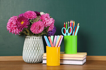 Stack of books, stationery and bouquet on wooden table against chalkboard © New Africa