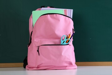Backpack with notebooks and stationery on white desk against chalkboard © New Africa