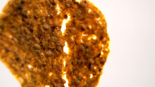 Backlit dehydrated fruit and seed crisp showing fibrous texture, macro rotating