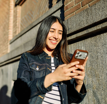 Portrait of a happy young woman tourist travelling or student or a businesswoman entrepreneur, using a smartphone phone or texting outdoors in front of a modern urban background