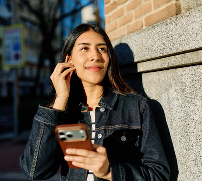 Young woman smiling, watching a video on her phone, and listening to music with wireless earbuds